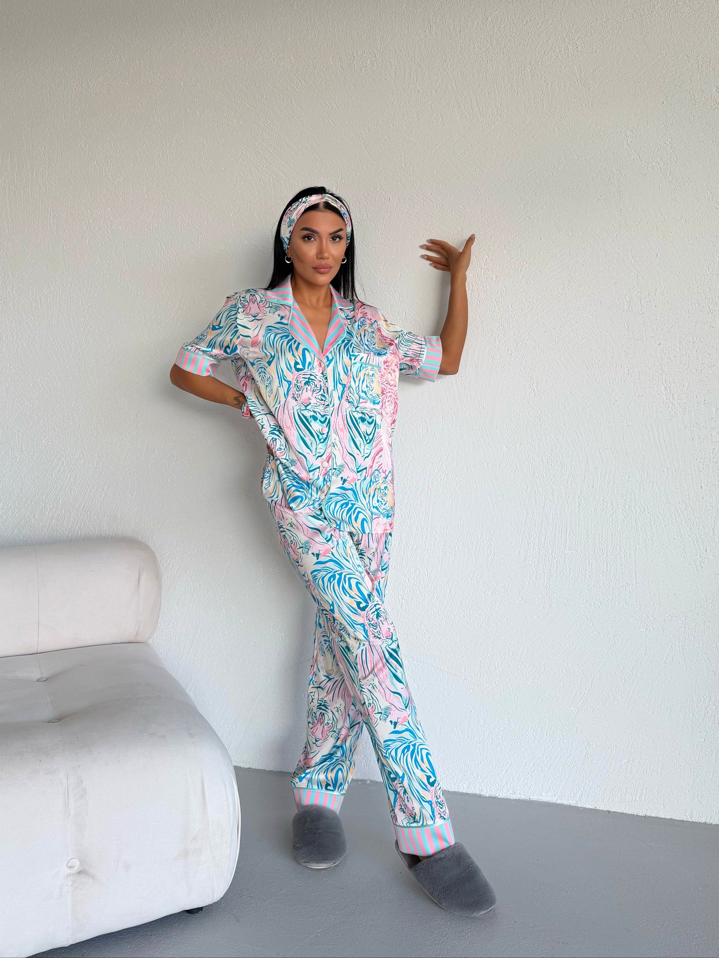 Woman wearing colorful tiger print pajama set with matching headband and gray slippers